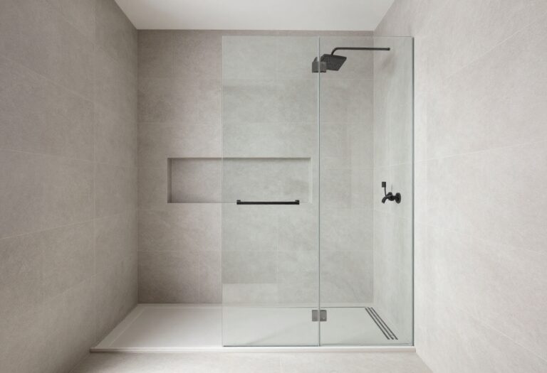Modern walk-in shower with large gray tile, frameless glass, and matte black fixtures.